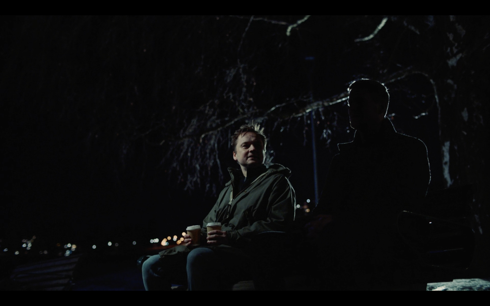 a man sitting next to a man holding a cup of coffee