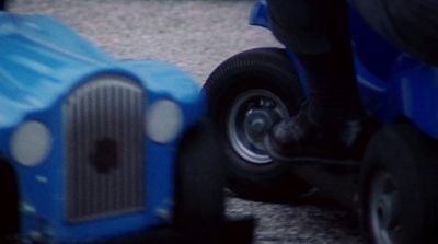 a person riding a blue toy car on a street