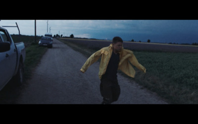 a man walking down a dirt road next to a car