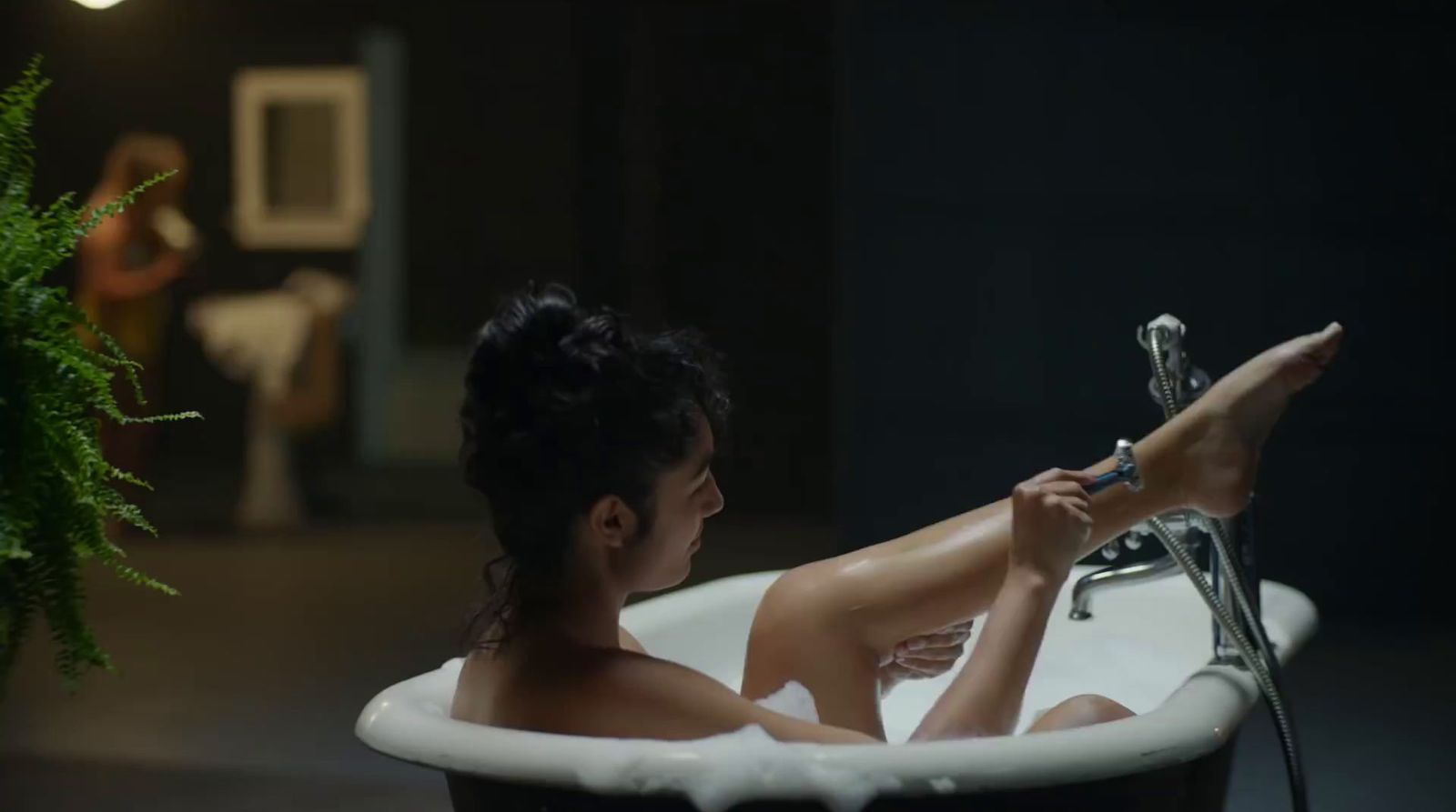 a woman sitting in a bathtub with a plant in the background