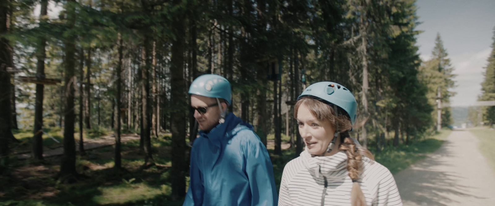 two people wearing helmets walking down a path in a forest