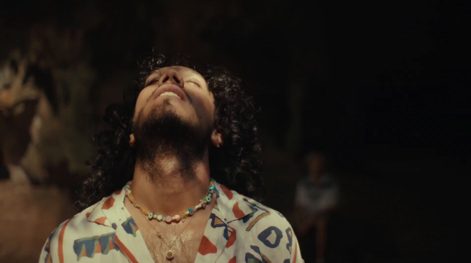 a man with long hair and a necklace looking up