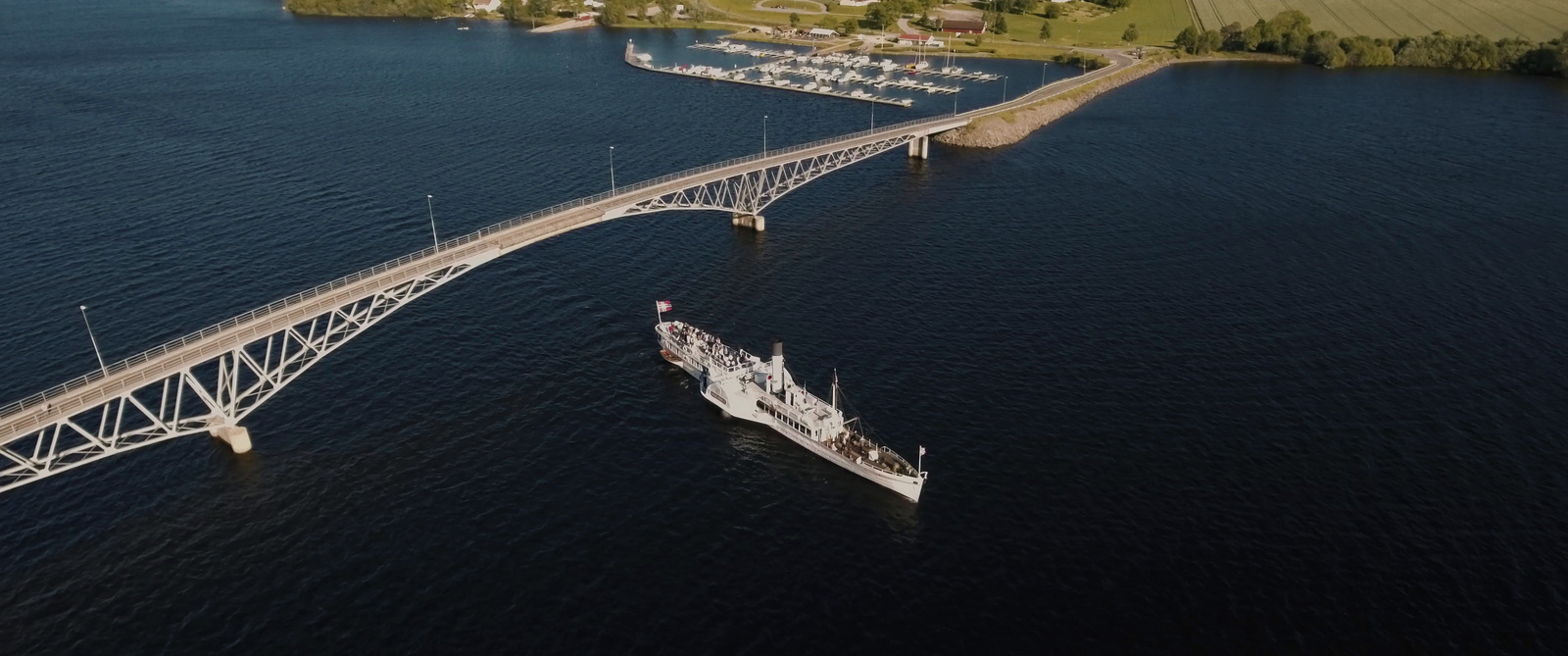 an aerial view of a ship passing under a bridge