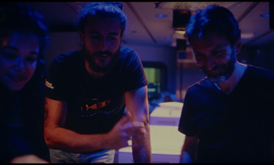 three men looking at a cell phone in a dark room