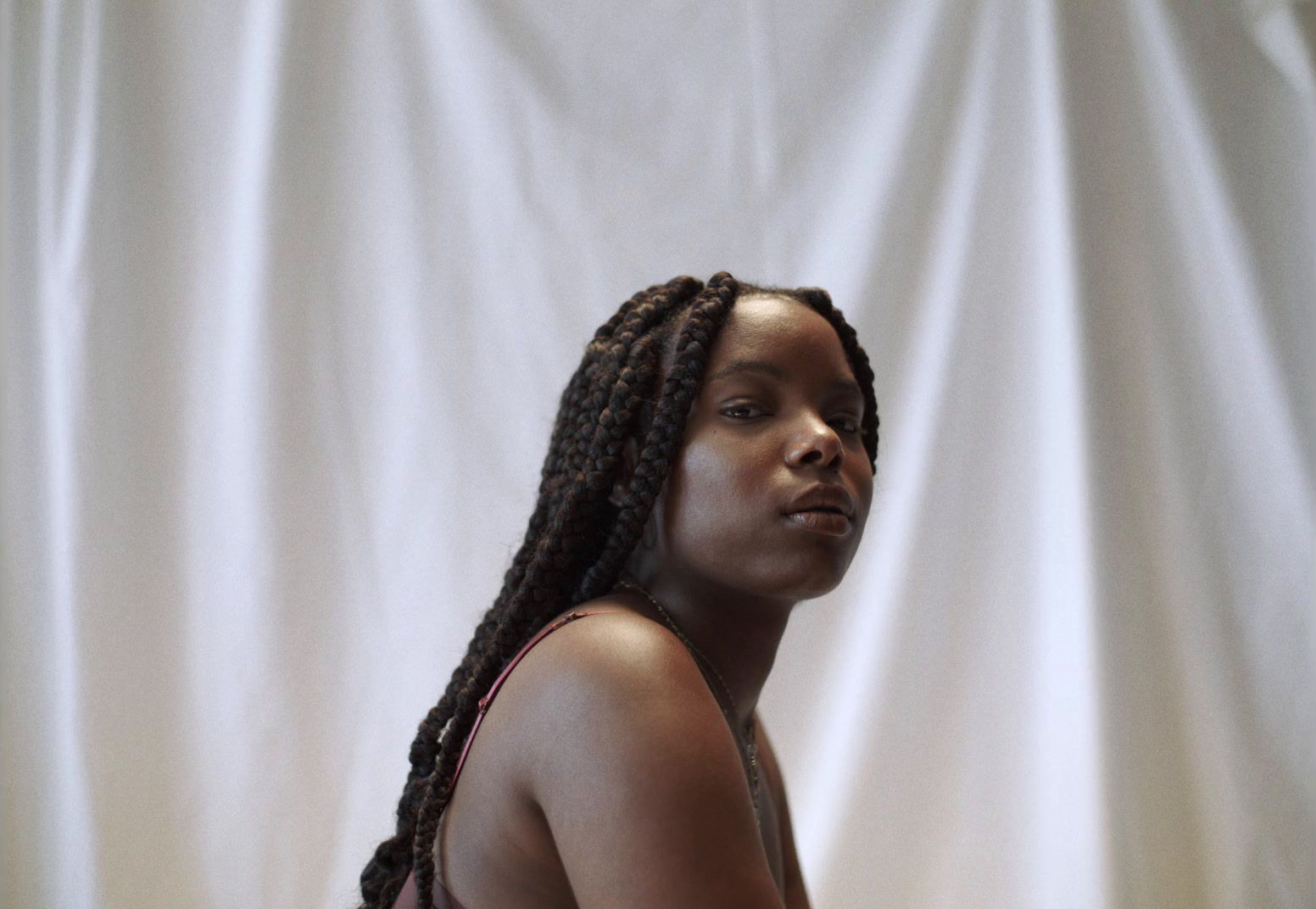 a woman with braids standing in front of a white curtain