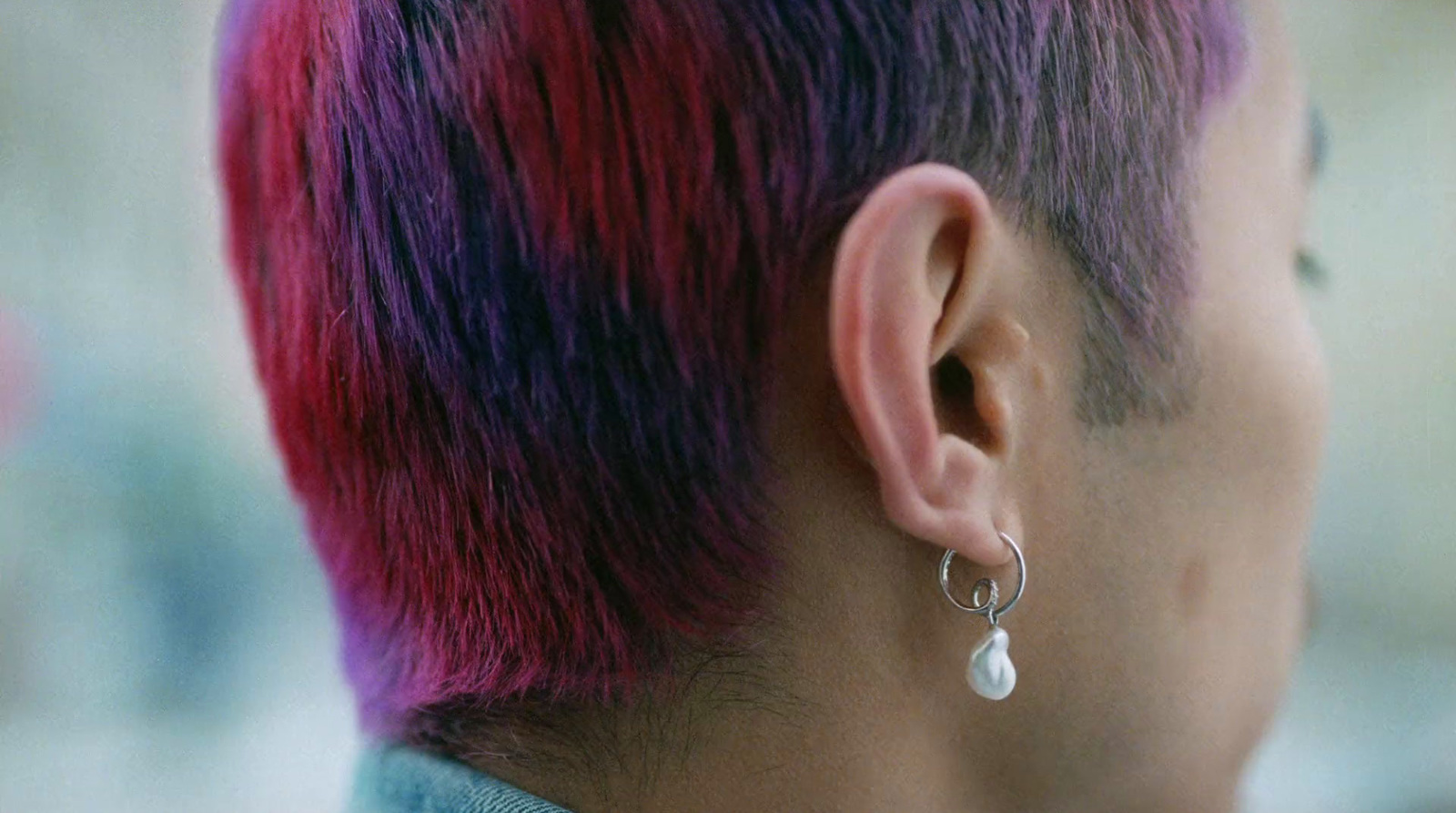 a man with pink hair wearing a pair of earrings