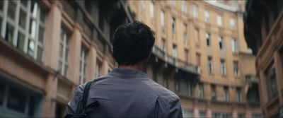 a man walking down a street past tall buildings