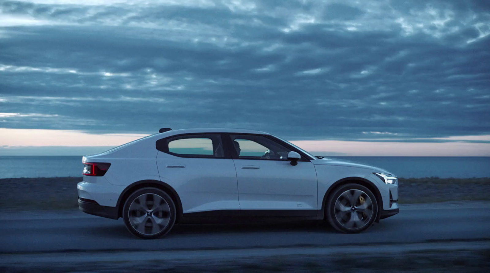 a white car driving down a road next to the ocean