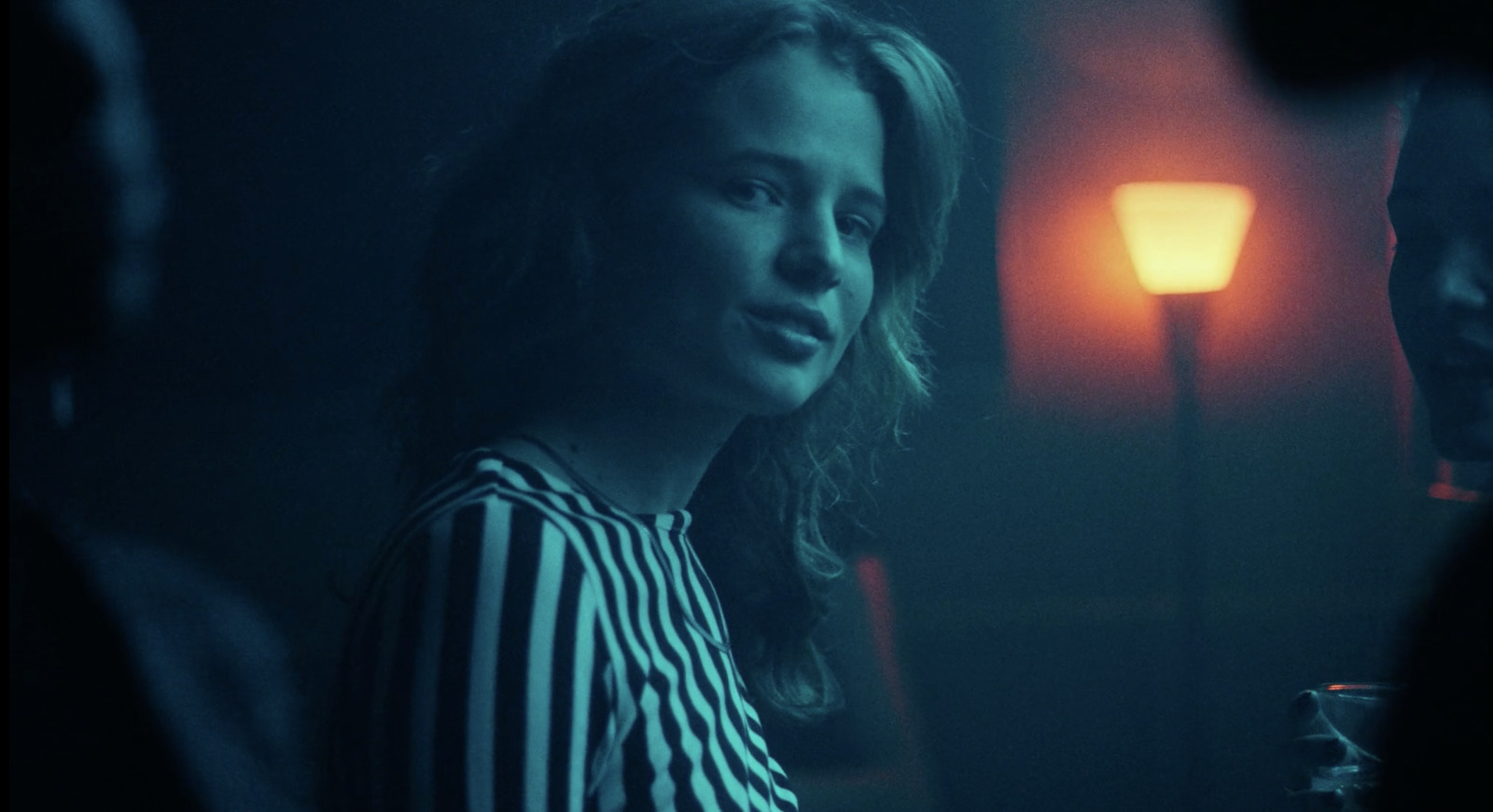 a woman standing in a dark room next to a lamp