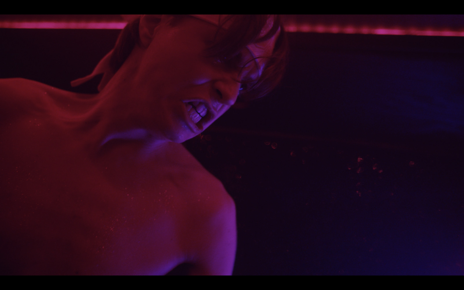 a shirtless man with his mouth open in a dark room