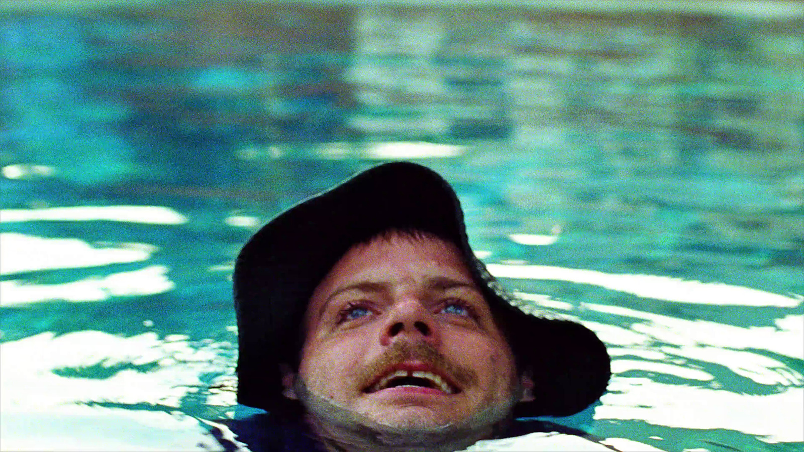 a man floating in a pool wearing a hat