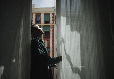 a man standing in front of a window with a shadow on the curtain