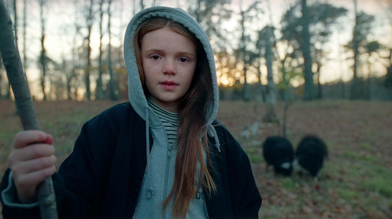 a young girl holding a stick in a forest