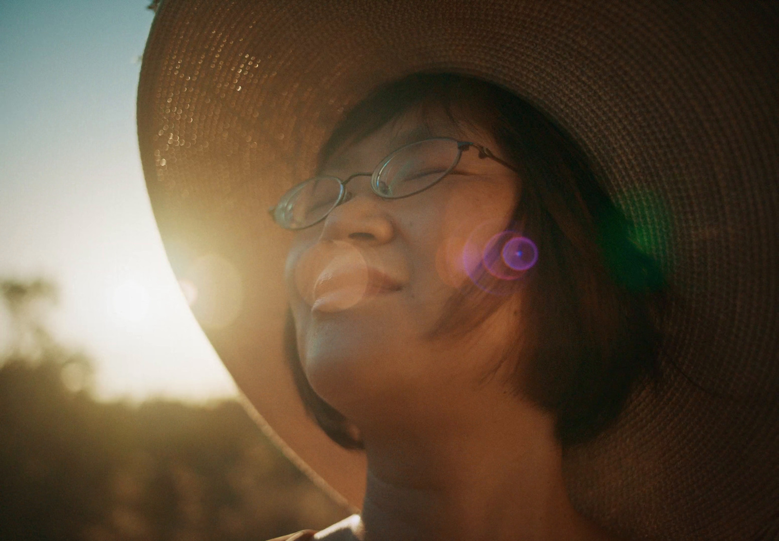 a woman wearing a hat and glasses looking up at the sky