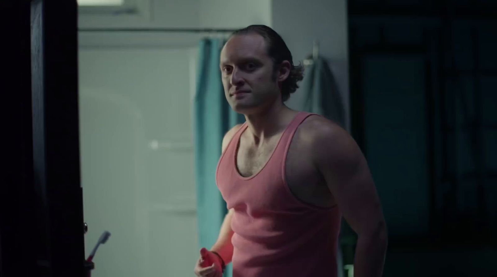 a man in a pink tank top holding a red object