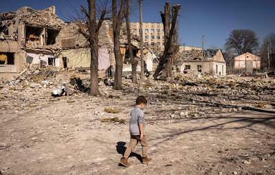 a young boy standing in the dirt in front of a destroyed building