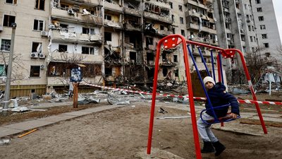 a child on a swing in front of a destroyed building