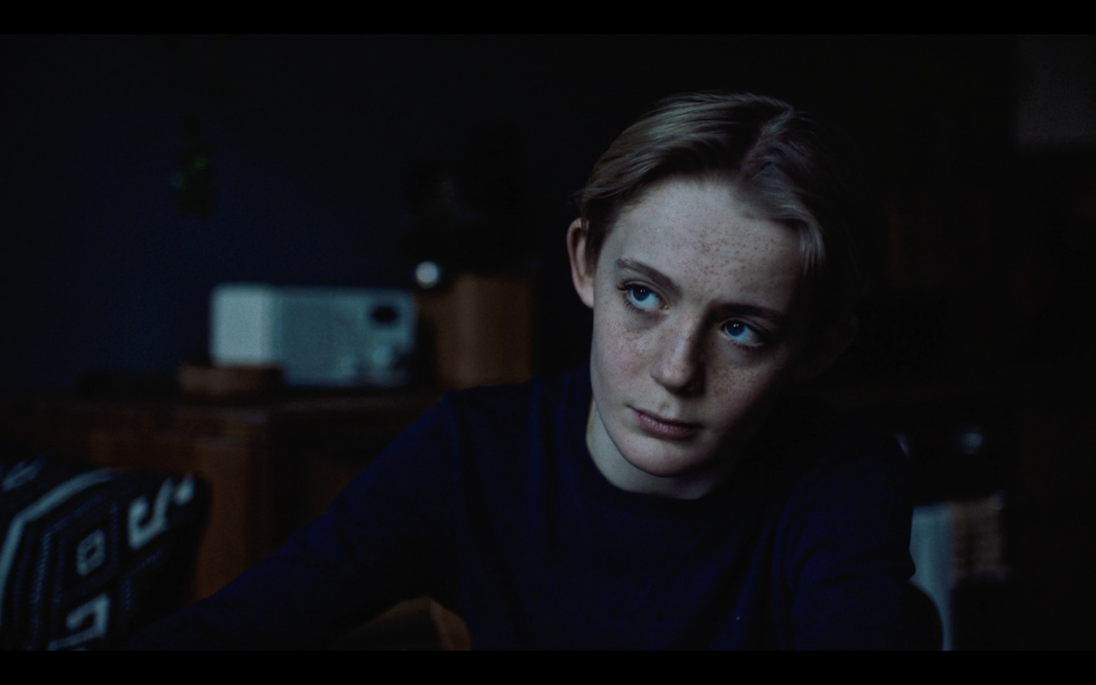 a woman sitting in a dark room looking at the camera