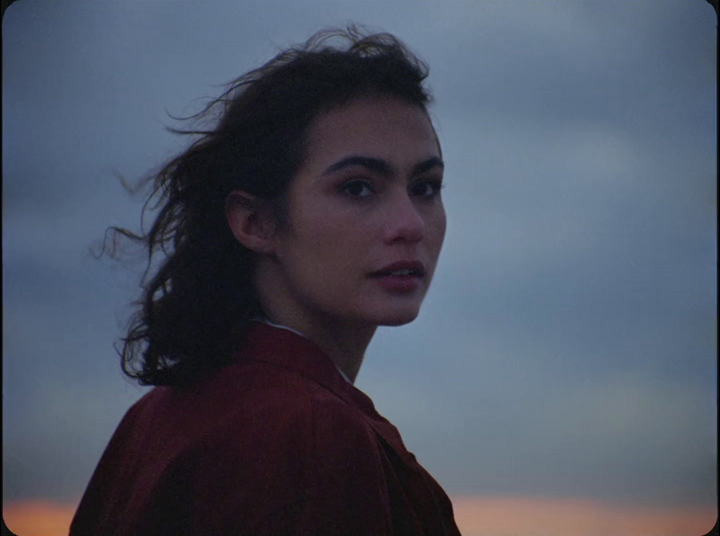 a woman with long hair standing in front of a cloudy sky