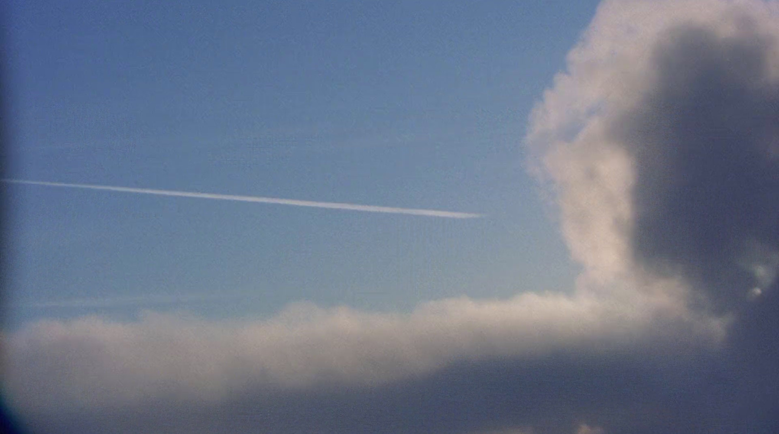 a plane flying in the sky with a contrail in the background