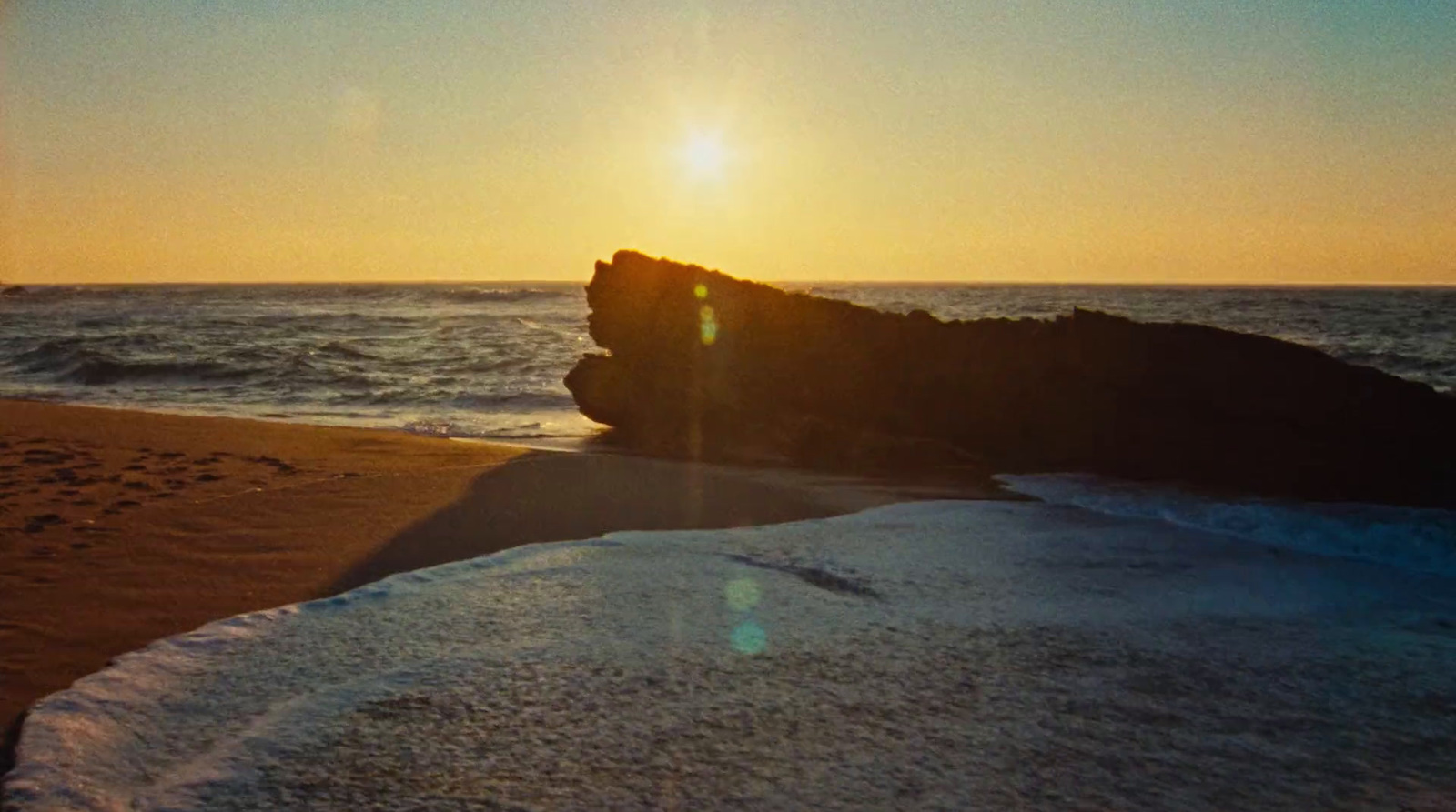 the sun is setting over the water on the beach