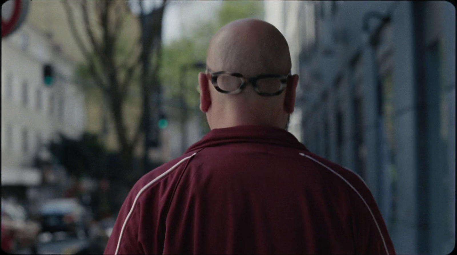 a bald man with glasses walking down a street