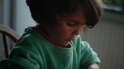 a young child sitting at a table using a cell phone