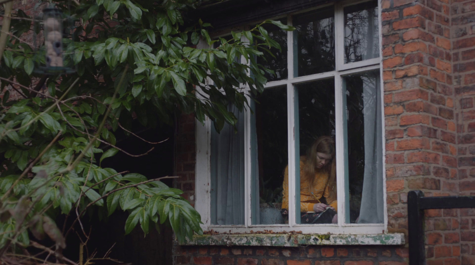 a woman in a yellow shirt looking out of a window