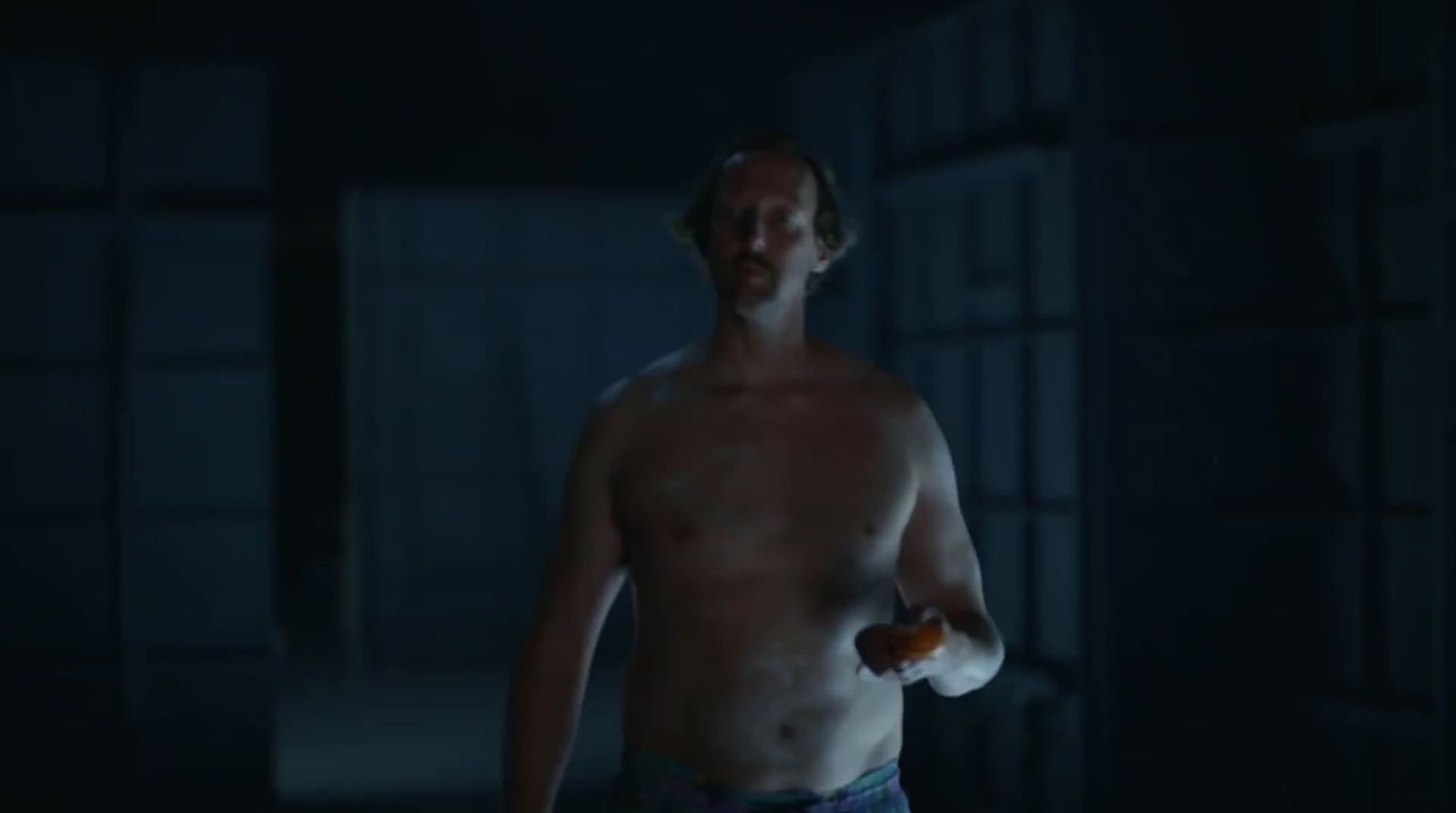 a shirtless man holding an apple in a dark room