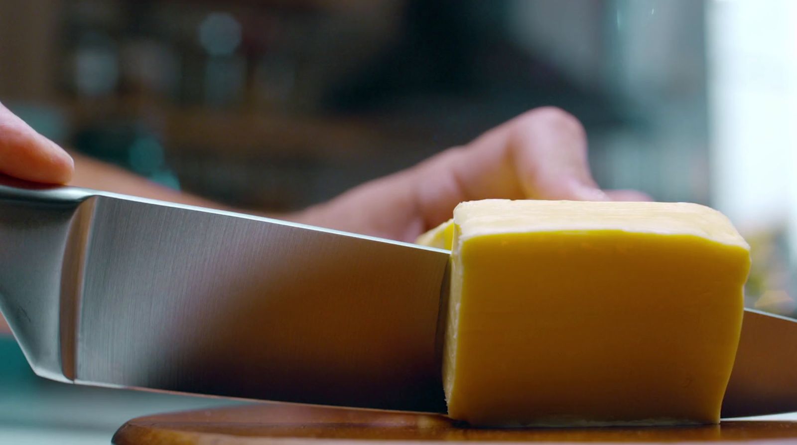 a person holding a knife over a block of cheese