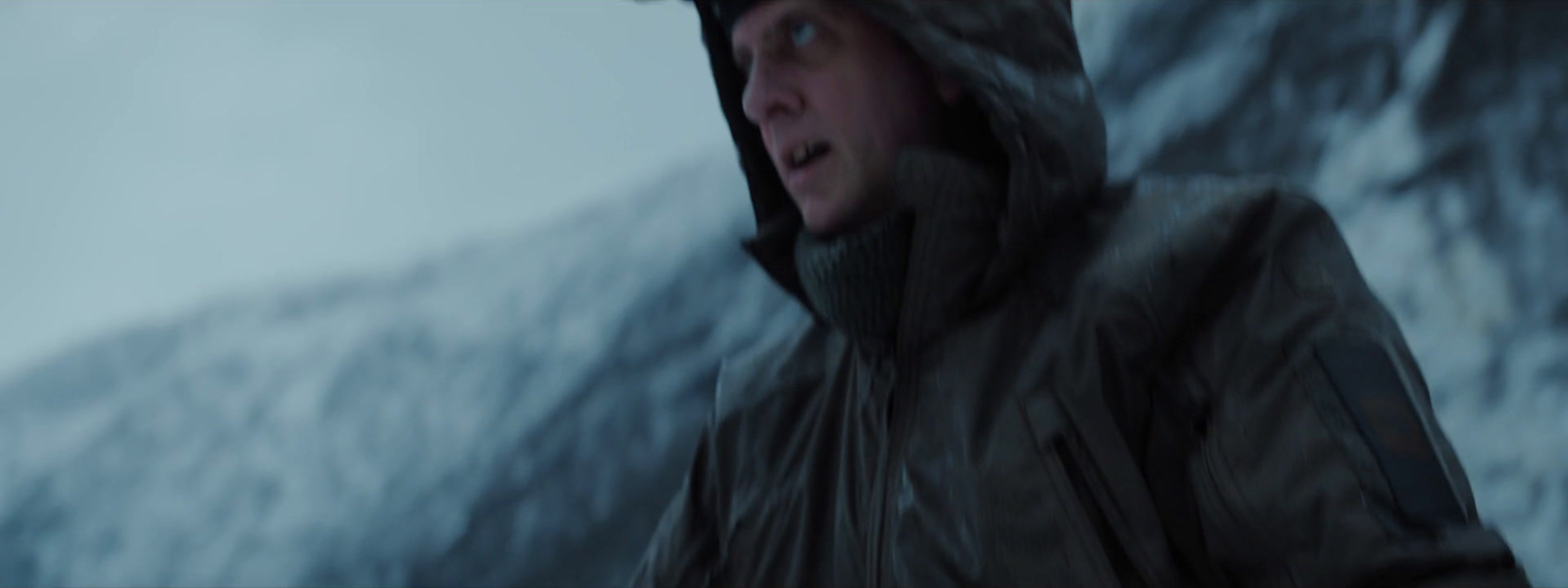 a man in a hooded jacket standing in front of a mountain