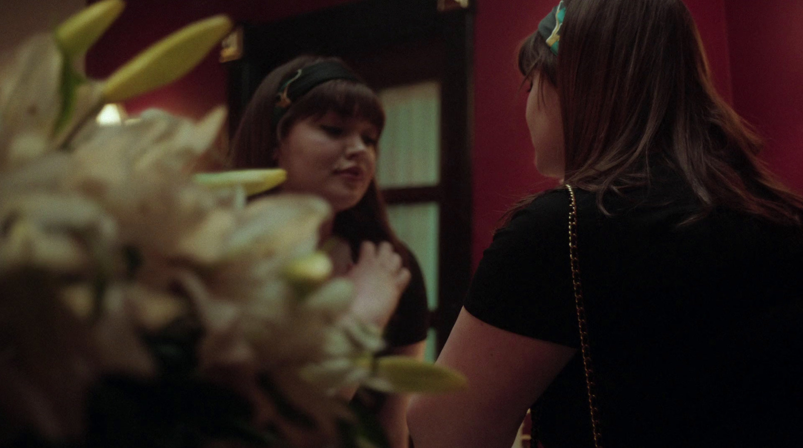 a woman standing in front of a mirror next to a vase of flowers