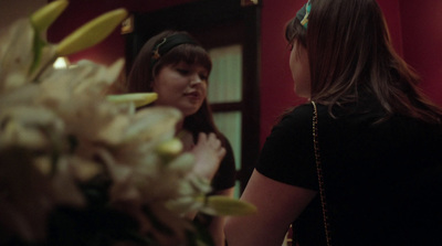 a woman standing in front of a mirror next to a vase of flowers