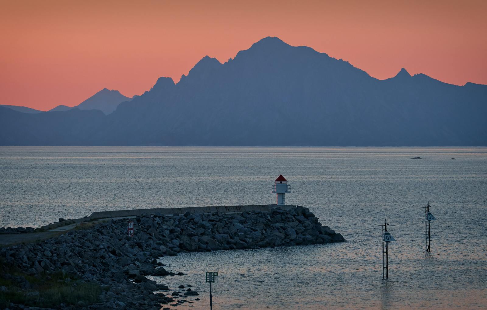 a lighthouse on a rocky shore with mountains in the background