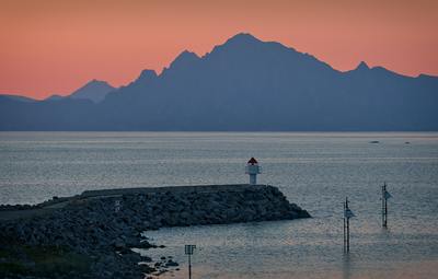 a lighthouse on a rocky shore with mountains in the background