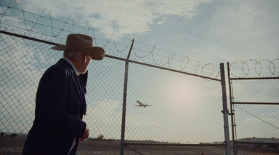 a man in a suit and hat standing in front of a fence