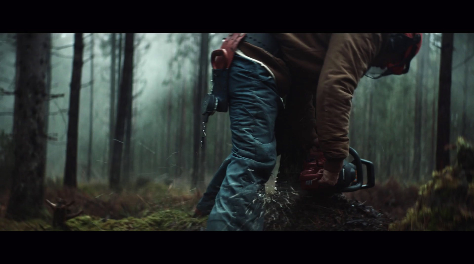 a man walking through a forest holding a chainsaw