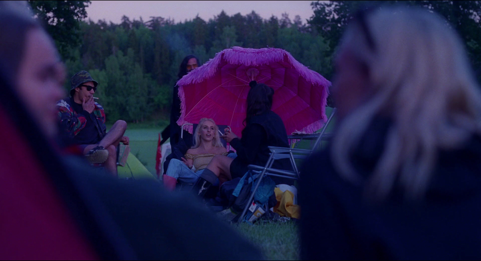 a group of people sitting around a pink umbrella