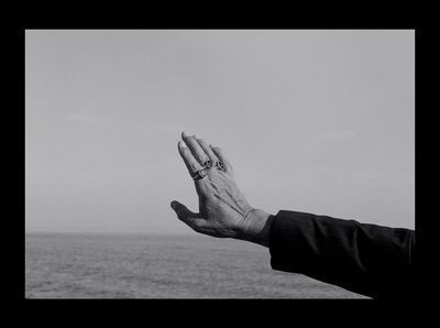 a person's hand reaching out towards the ocean