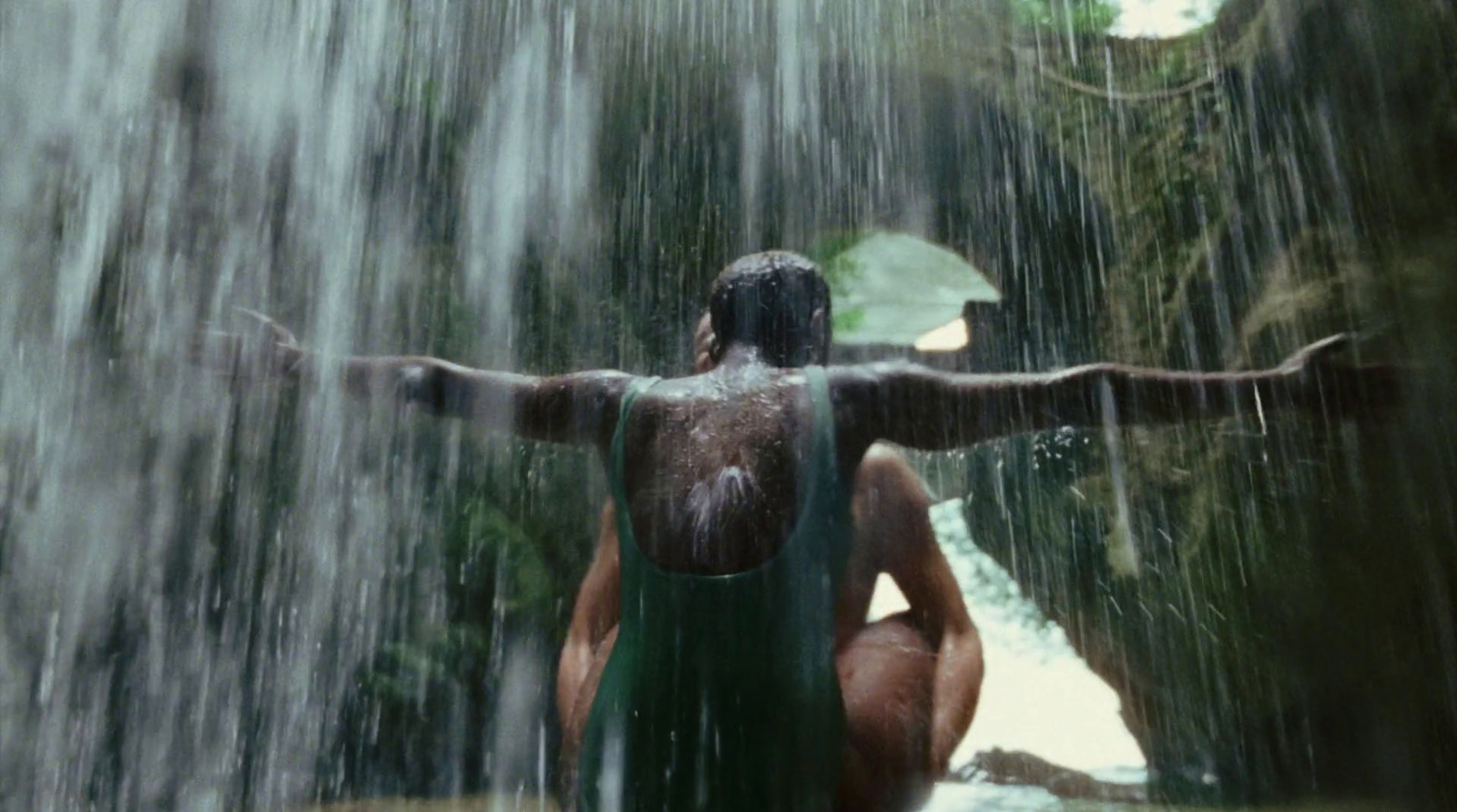 a woman in a green bathing suit sitting under a waterfall