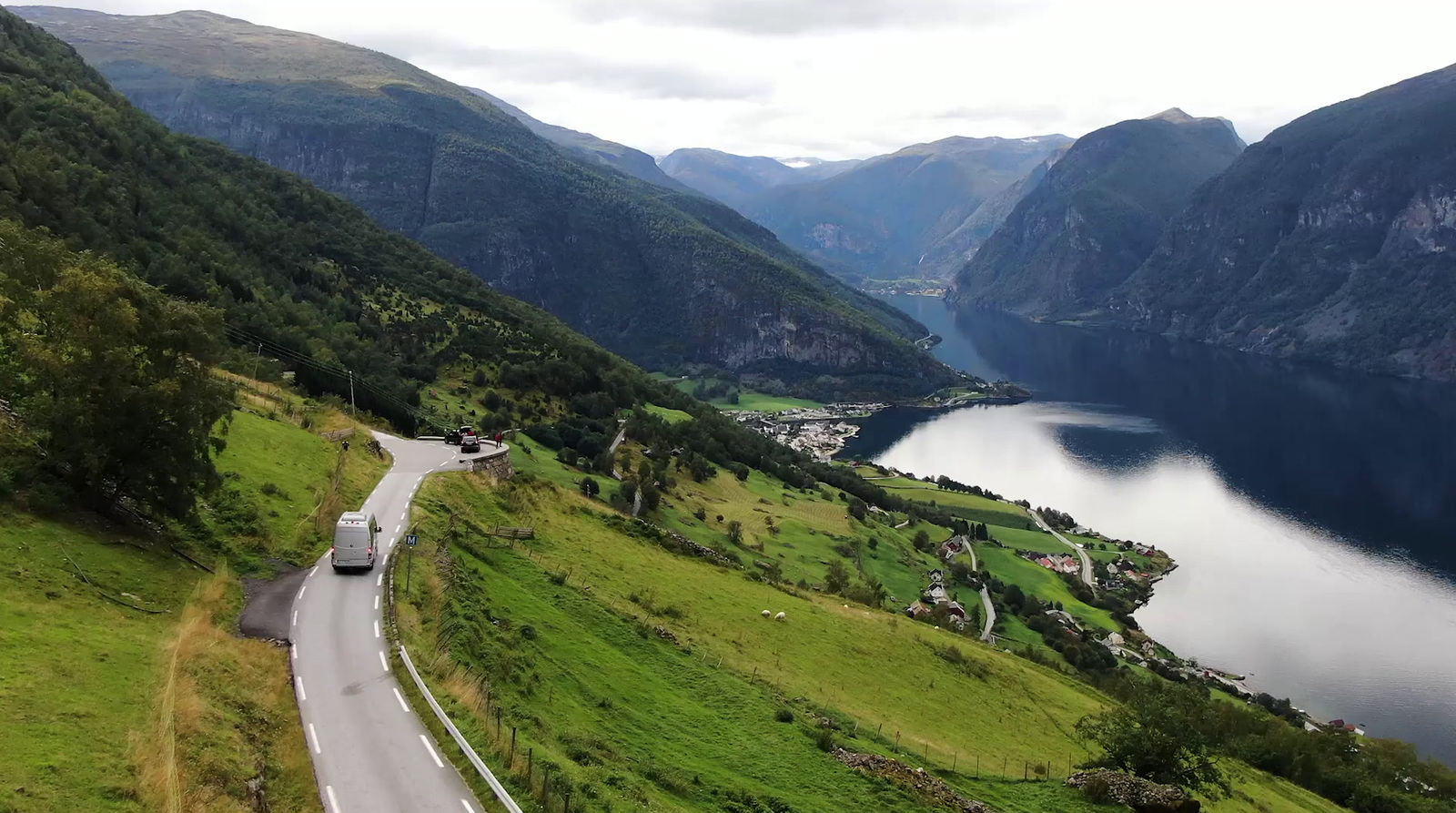 a car driving down a mountain road near a lake