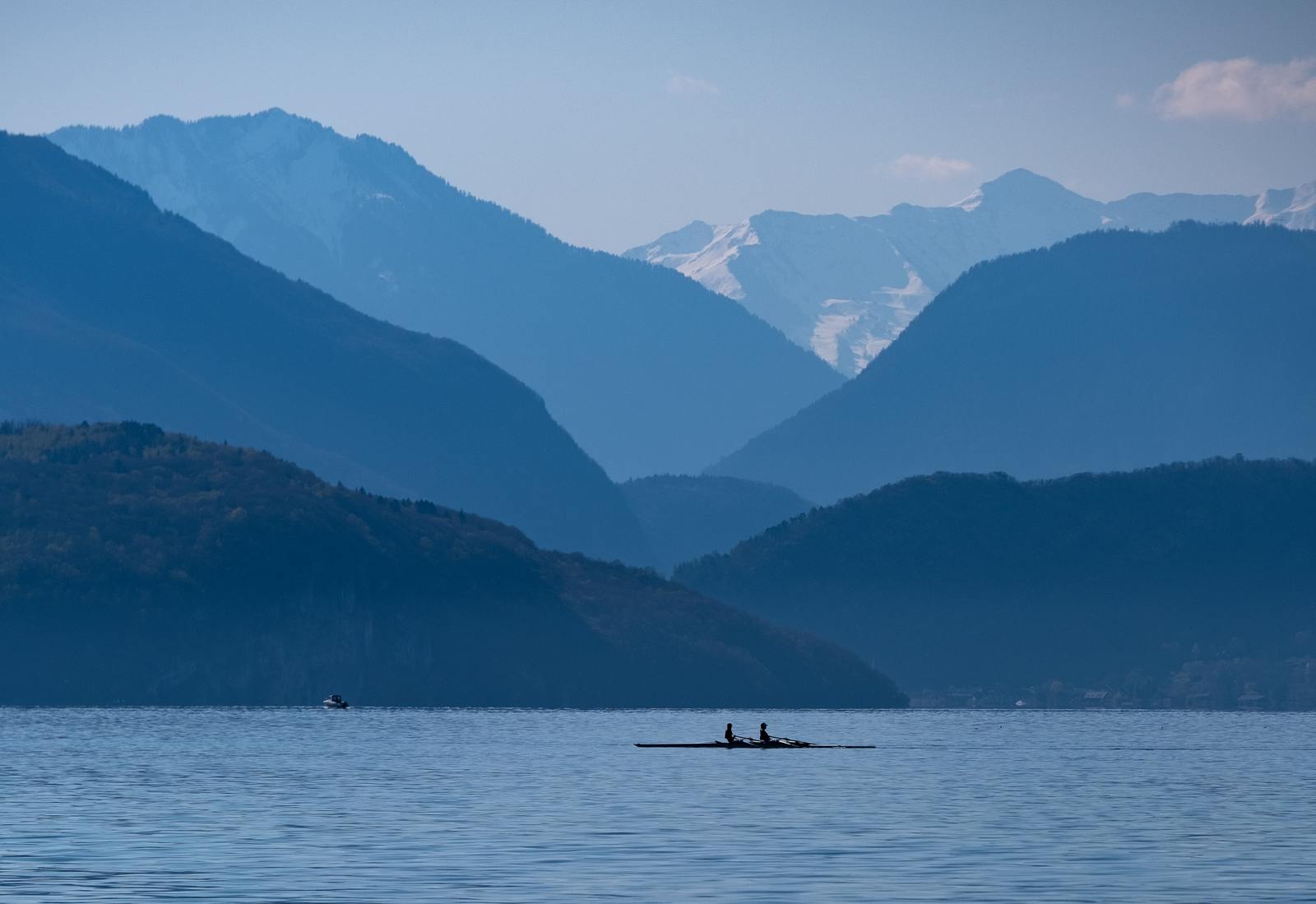 two people are rowing in the water with mountains in the background