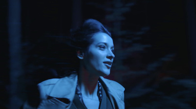 a woman in a jacket and tie standing in the dark