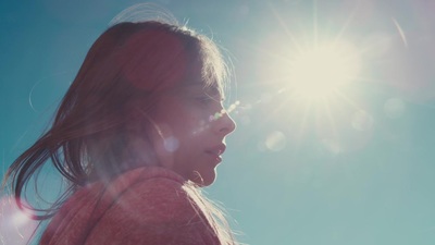 a woman standing in the sun with her hair blowing in the wind