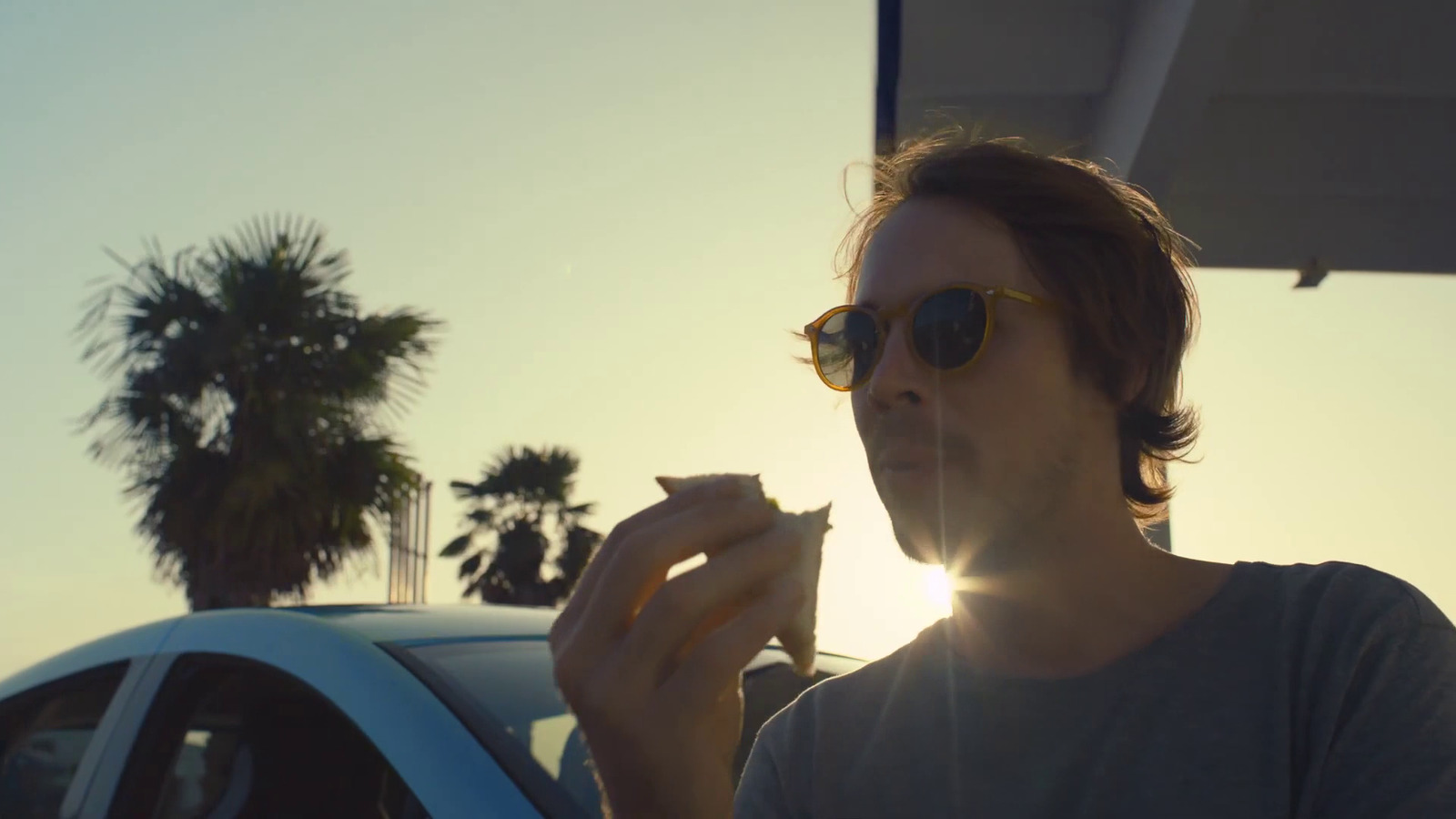 a man in sunglasses eating a donut in front of a car