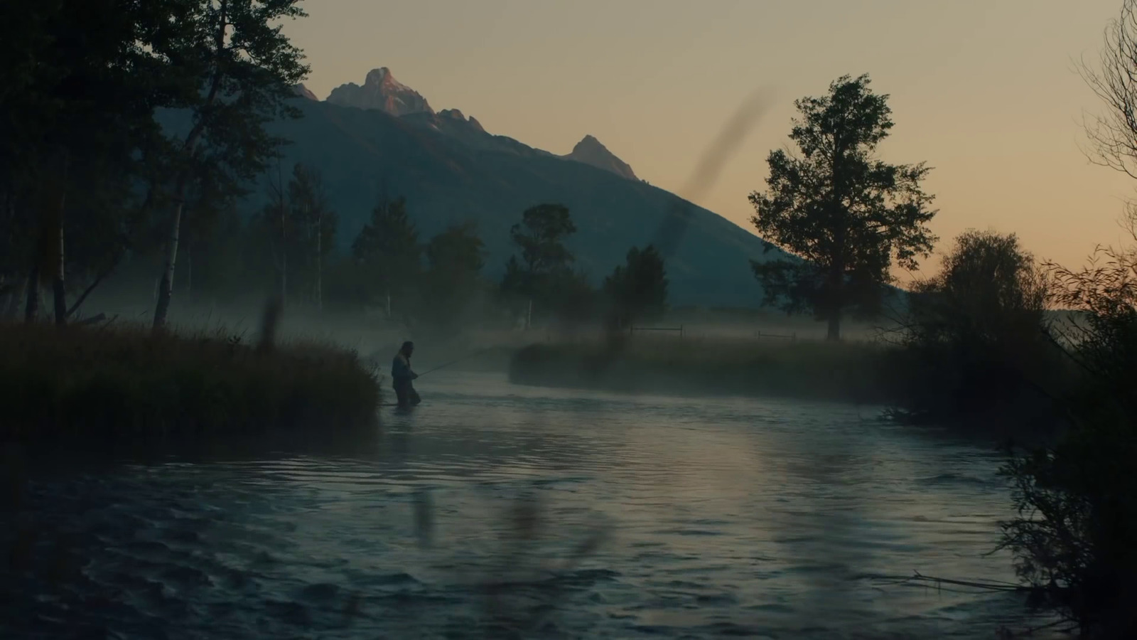 a man fishing in a river at sunset