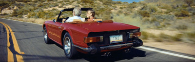 a man and woman riding in the back of a red convertible