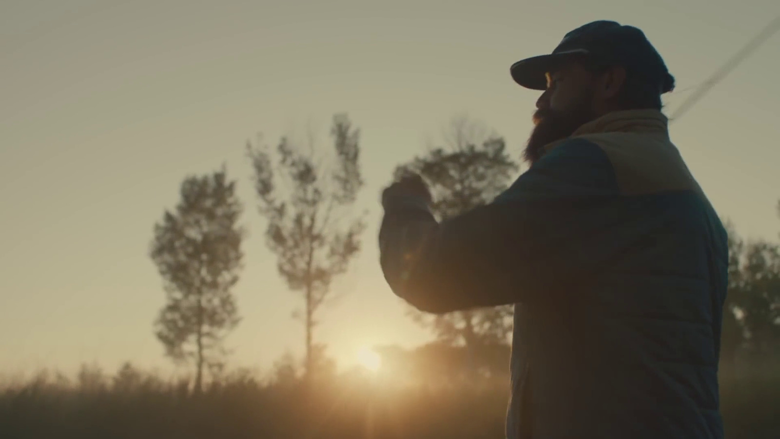 a man standing in a field with the sun setting behind him