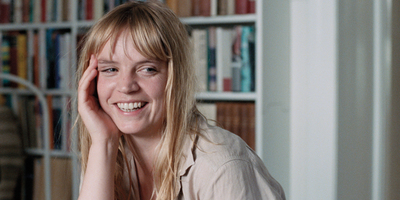 a woman sitting in front of a bookshelf smiling