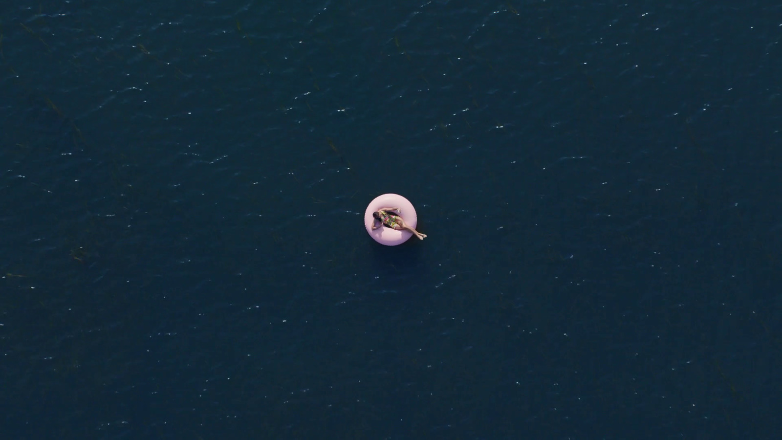 an aerial view of a person floating on a pink object in the water